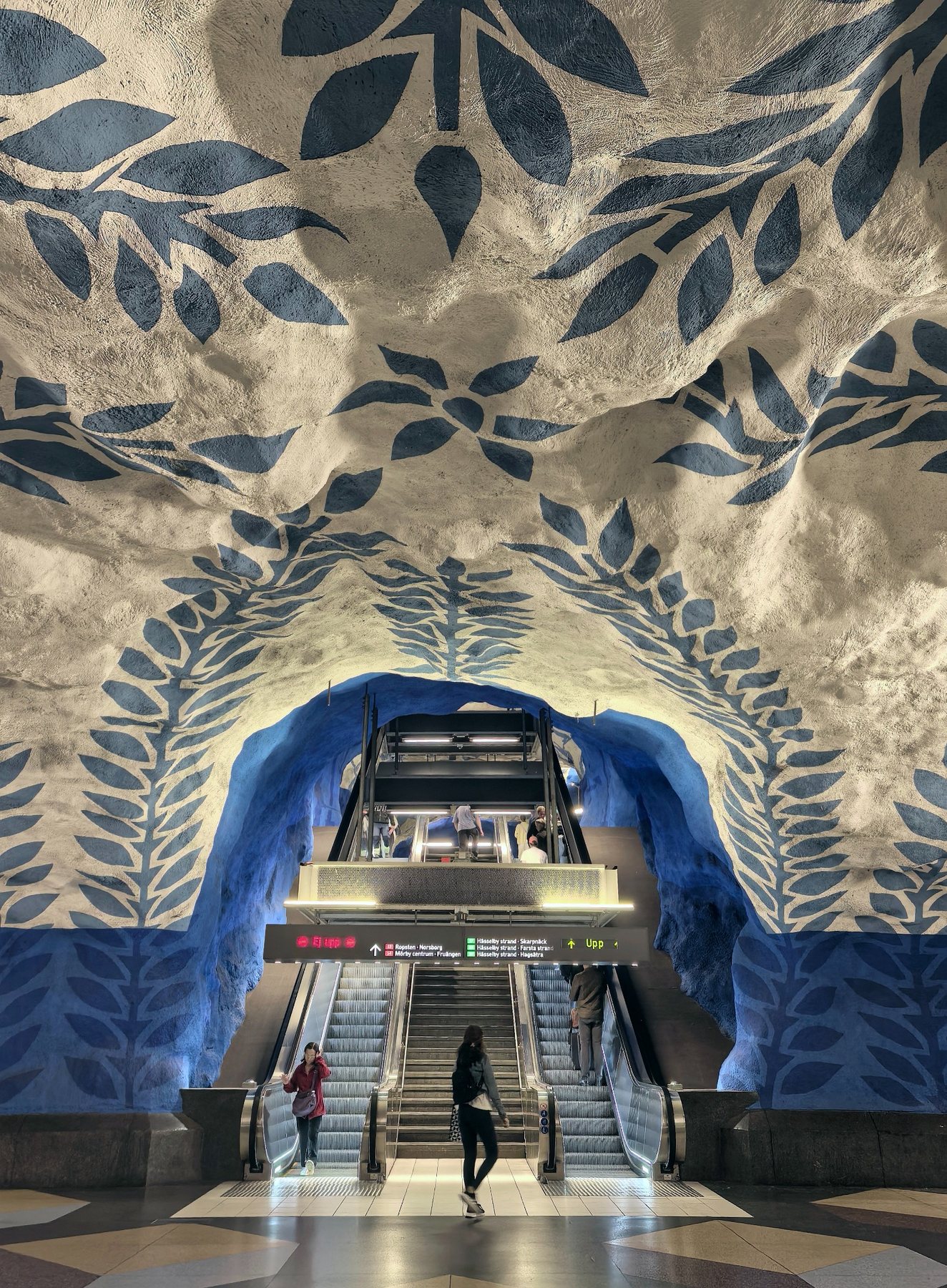 A blue-and-white underground station interior with escalators.
