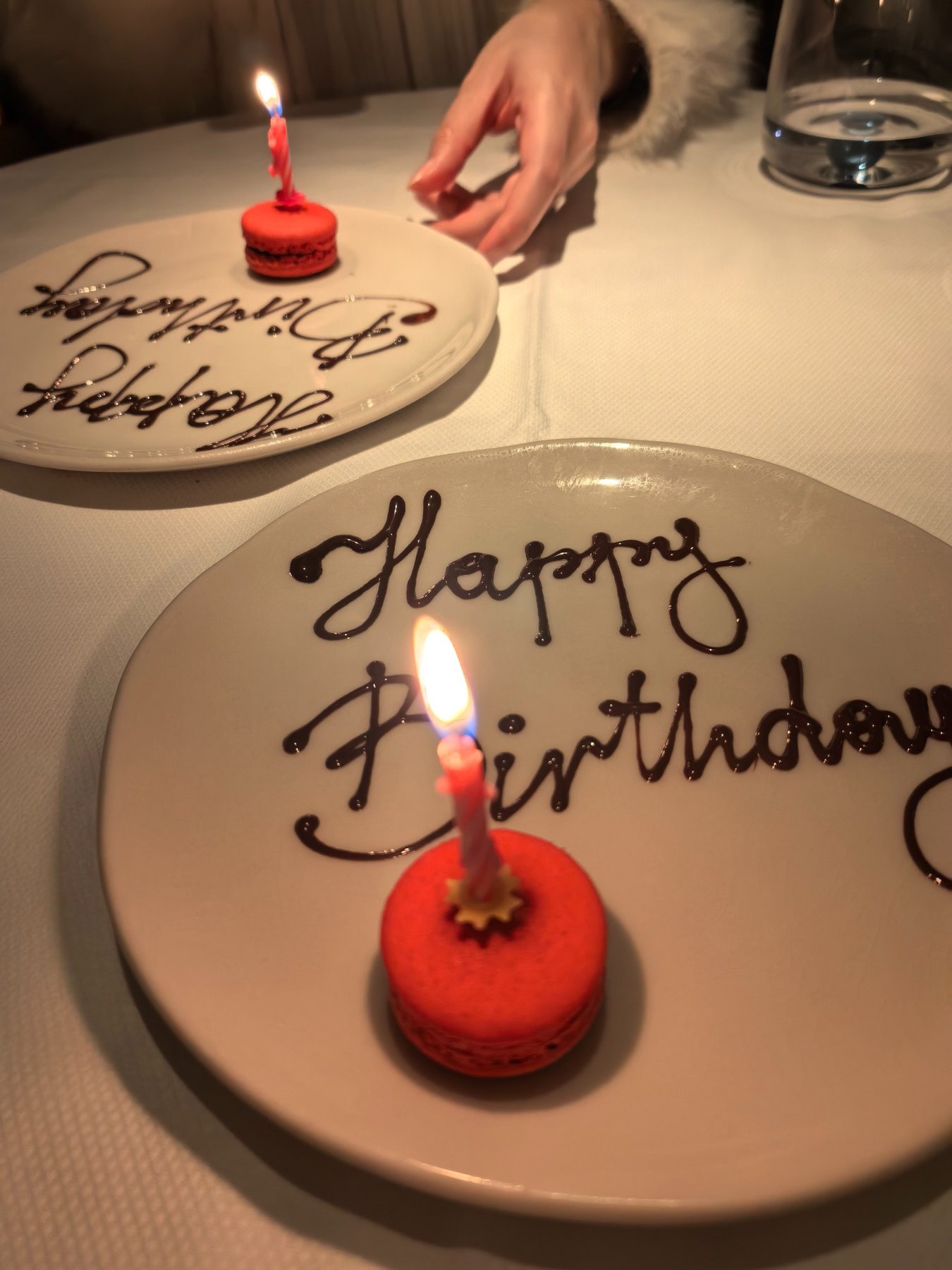 Two small birthday desserts with lit candles on white plates.