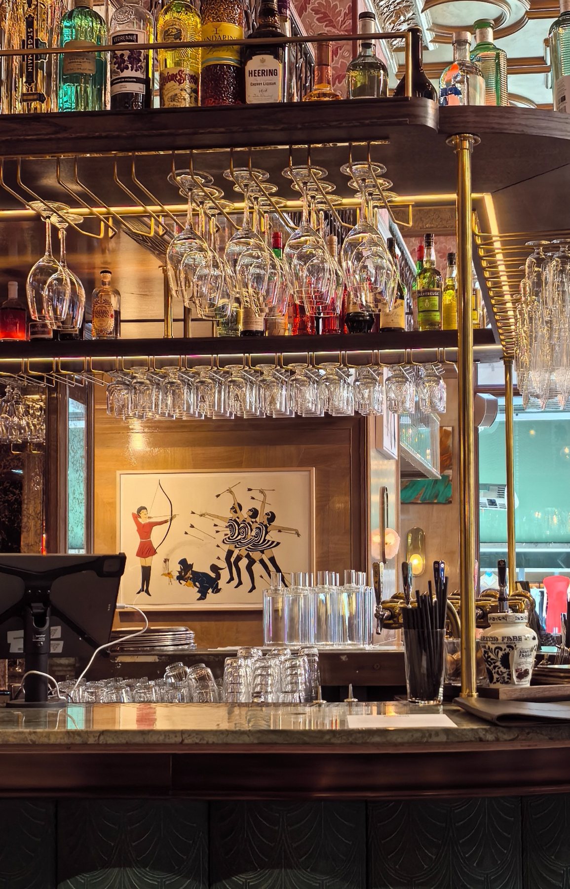 A bar interior with hanging glasses and a framed artwork.