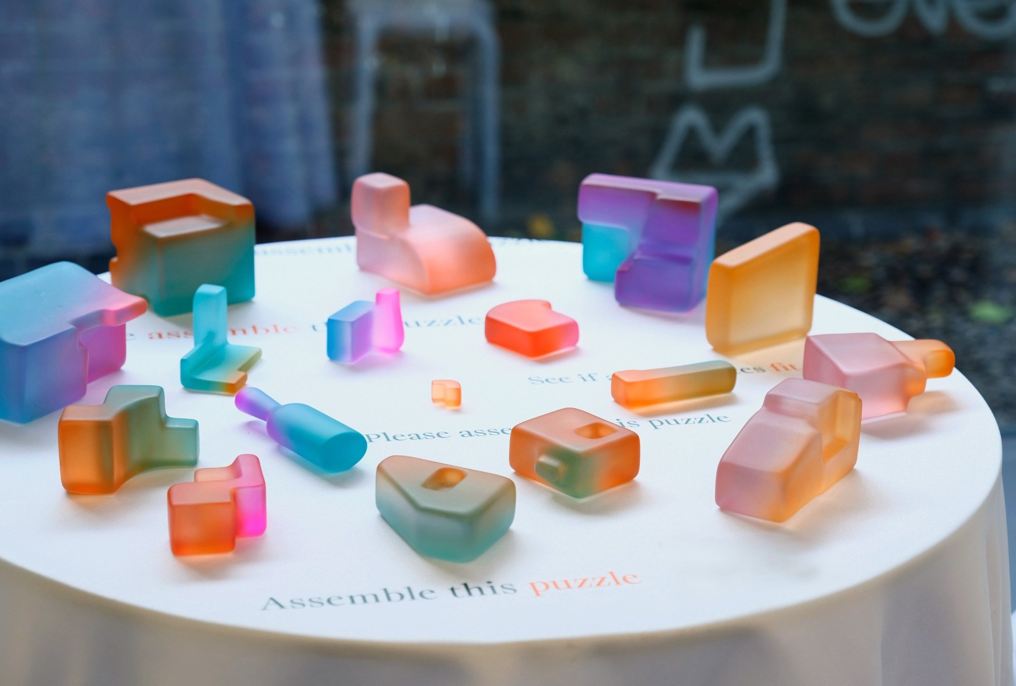 Translucent, brightly coloured sculptural fragments arranged across a round table.